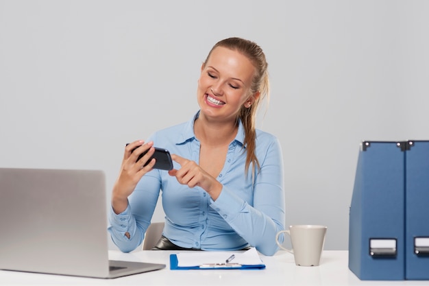 Szczęśliwa kobieta za pomocą telefonu komórkowego podczas pracy biurowej