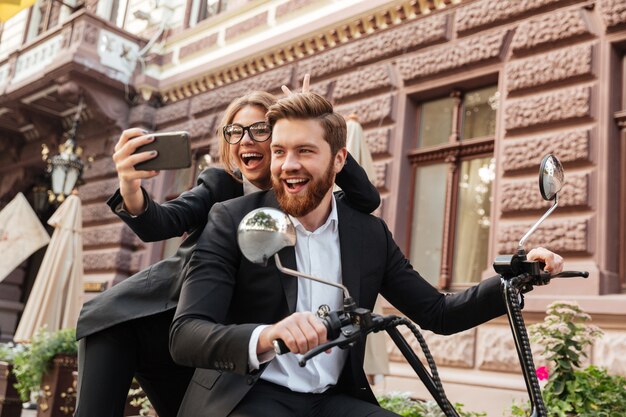 Bezpłatne zdjęcie szczęśliwa krzycząca elegancka para siedzi na nowożytnym motocyklu outdoors