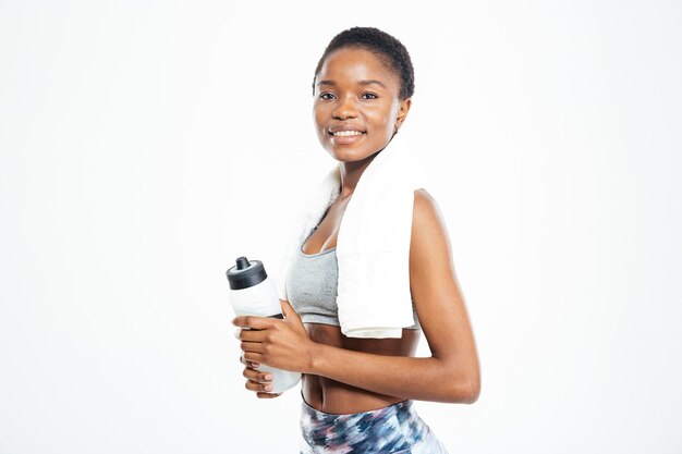Szczęśliwa ładna młoda afroamerykańska sportsmenka z ręcznikiem i butelką wody