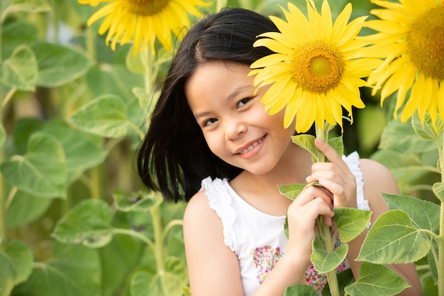 szczęśliwa mała azjatycka dziewczyna bawi się wśród kwitnących słoneczników pod delikatnymi promieniami słońca.