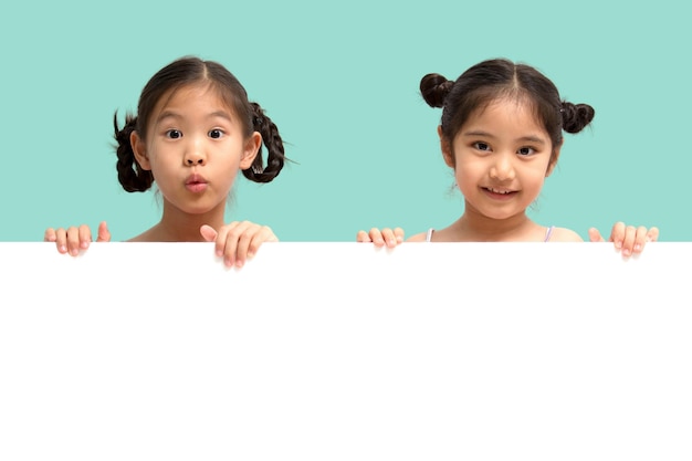 Szczęśliwa mała azjatycka dziewczynka uśmiecha się i pokazuje biały pusty znak billboard na pastelowym zielonym tle