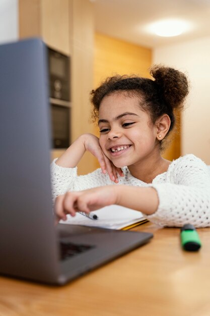 Szczęśliwa mała dziewczynka w domu podczas szkoły online z laptopem