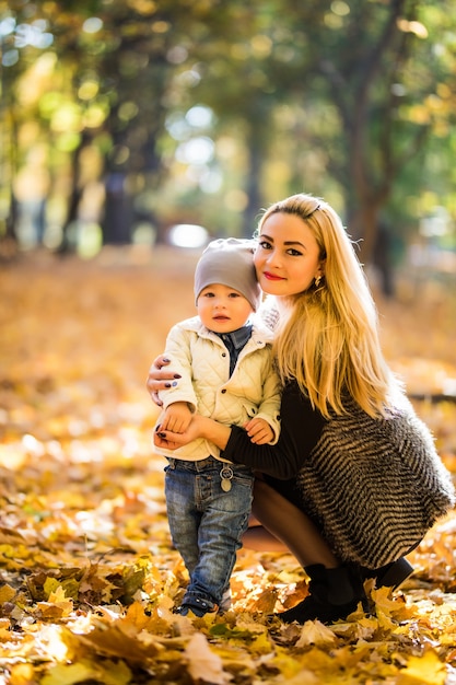 Szczęśliwa matka bawi się z dzieckiem w parku jesienią. Dziecko uśmiecha się do mamy na rękach