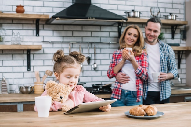 Szczęśliwa matka i córka patrzeje ich dzieciaka używa cyfrową pastylkę w kuchni