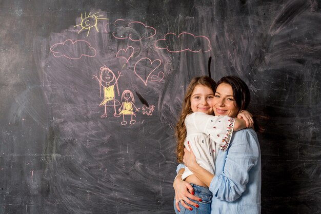 Szczęśliwa matka i córka ściska blisko chalkboard z rysunkiem