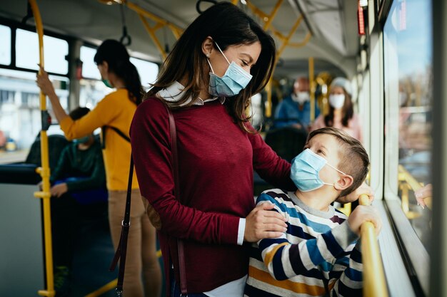 Szczęśliwa matka i syn rozmawiają podczas dojazdów autobusem i noszą ochronne maski na twarz