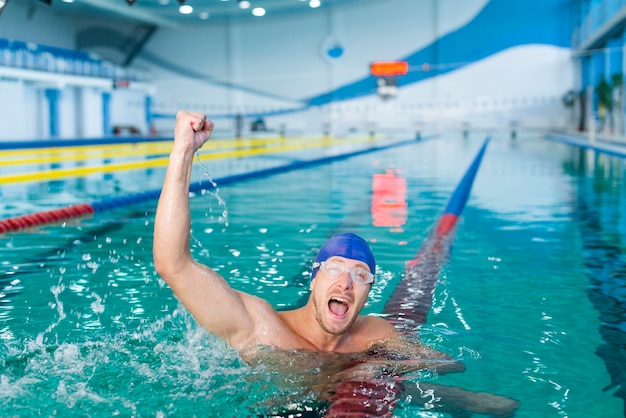 Bezpłatne zdjęcie szczęśliwa męska pływaczki dźwigania ręka w wodzie