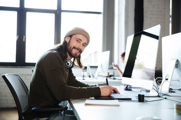 Szczęśliwa mężczyzna praca pozuje w biurze z komputerem.