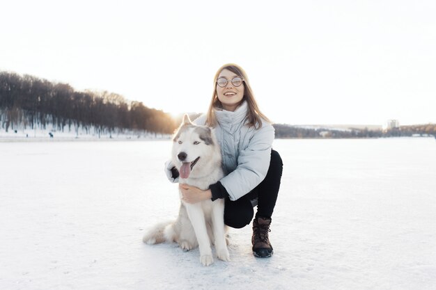 Szczęśliwa młoda dziewczyna bawić się z siberian husky psem w zima parku