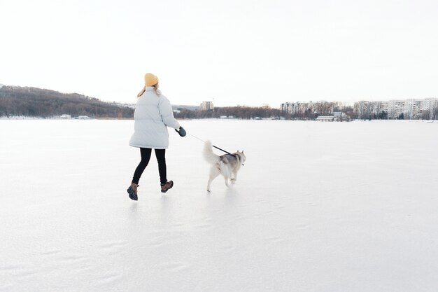 Szczęśliwa młoda dziewczyna bawić się z siberian husky psem w zima parku