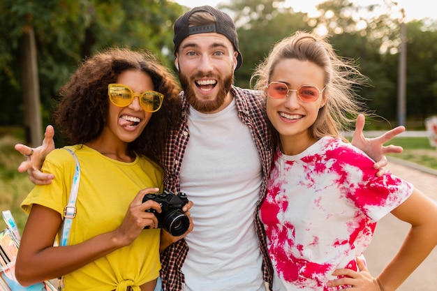 Szczęśliwa młoda firma emocjonalnych uśmiechniętych przyjaciół spaceru w parku z aparatem fotograficznym, mężczyzny i kobiety, bawiące się razem