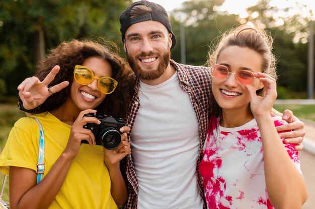 Szczęśliwa młoda firma emocjonalnych uśmiechniętych przyjaciół spaceru w parku z aparatem fotograficznym, mężczyzny i kobiety, bawiące się razem