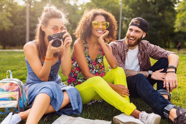 Szczęśliwa młoda firma rozmawiających uśmiechniętych przyjaciół siedzących w parku, mężczyzny i kobiety, wspólnej zabawy, podróżowanie z aparatem