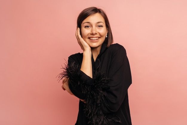 Szczęśliwa młoda kaukaska brunetka z uśmiechem na twarzy patrzy na kamerę na różowym tle Koncepcja stylu życia