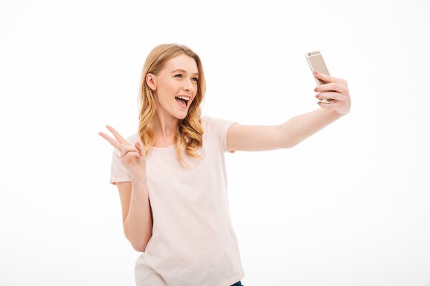 Szczęśliwa młoda kobieta bierze selfie z pokoju gestem.