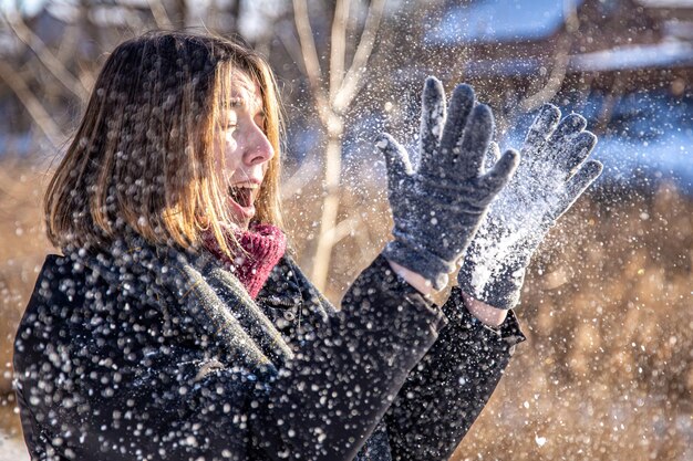 Szczęśliwa młoda kobieta na spacerze zimą ze śniegiem w dłoniach