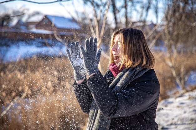 Szczęśliwa młoda kobieta na spacerze zimą ze śniegiem w dłoniach