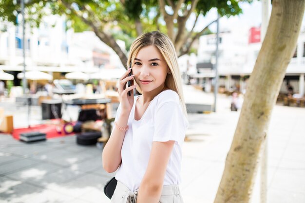 Szczęśliwa młoda kobieta rozmawia telefon na portret ulicy stylu życia miasta w okresie letnim