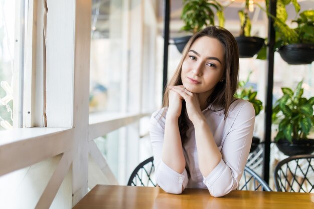 Szczęśliwa młoda kobieta siedzi i czeka na porządek w kawiarni