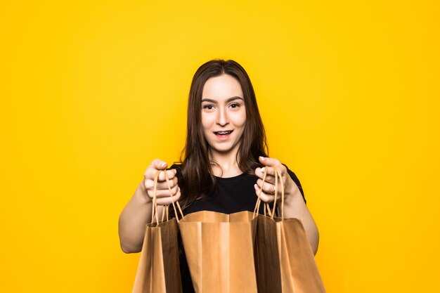 Szczęśliwa młoda kobieta trzymając torby na zakupy na żółtej ścianie