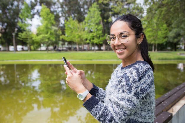 Szczęśliwa młoda kobieta używa smartphone w parku