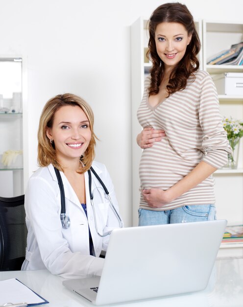 Szczęśliwa młoda kobieta w ciąży i jej lekarz z laptopem