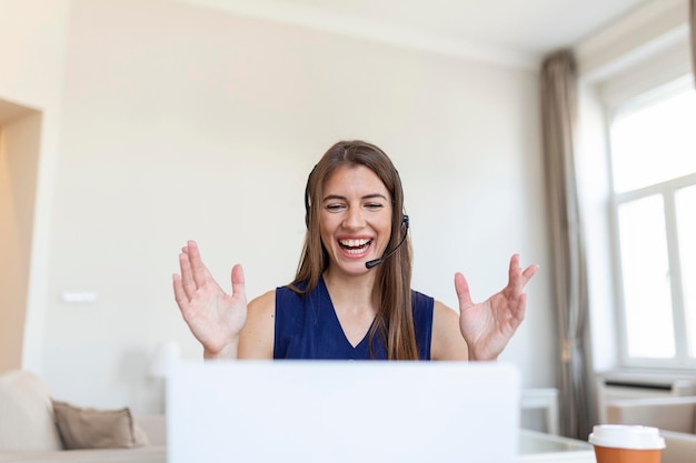 Szczęśliwa młoda kobieta w słuchawkach mówiąca patrząc na laptopa robiąca notatki biznesowa kobieta rozmawiająca przez wideokonferencję Konferencja przez kamerę internetową koncepcja szkolenia online ecoaching