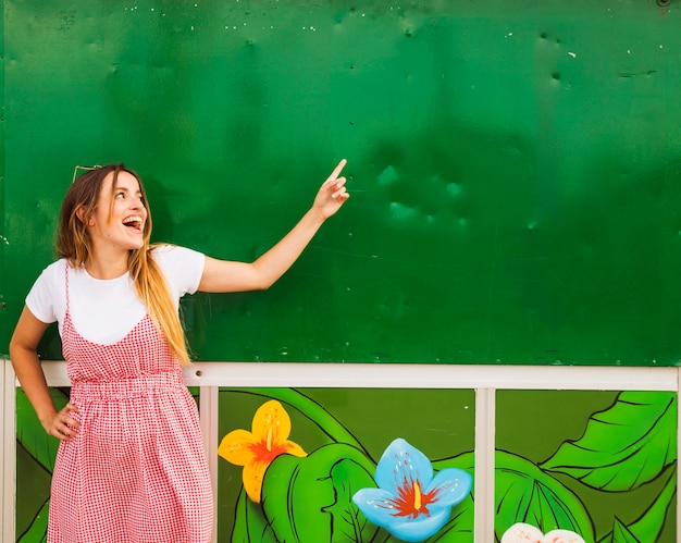 Szczęśliwa młoda kobieta wskazuje palec na zieleni ścianie