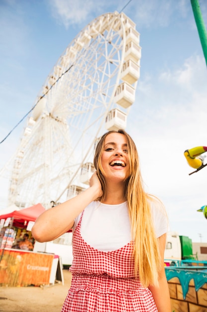 Bezpłatne zdjęcie szczęśliwa młoda kobieta z długą blondynka włosy pozycją przed ferris kołem
