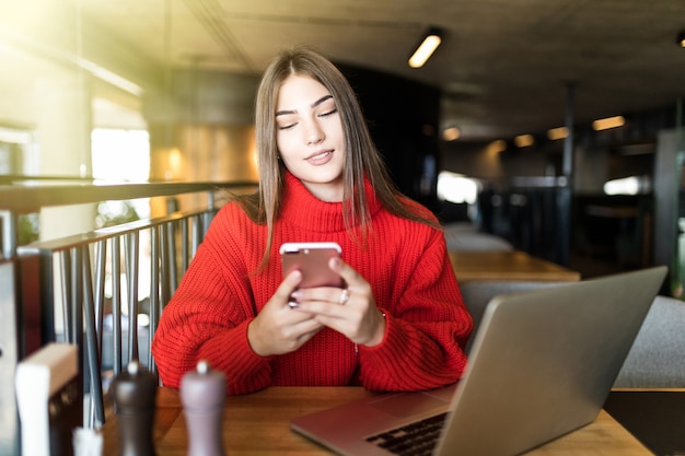 Szczęśliwa młoda kobieta za pomocą laptopa i smartfona w kawiarni