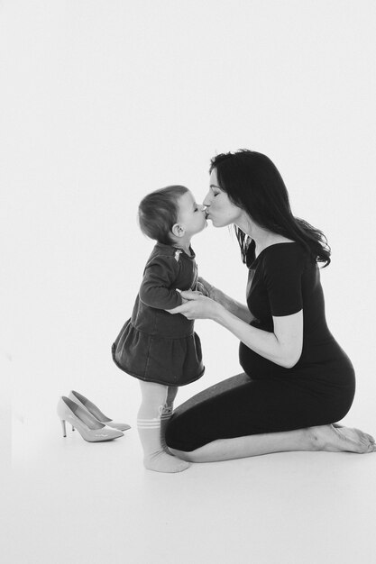 Szczęśliwa młoda mama w ciąży całuje swoje małe dziecko i przytula się z nią na białym tle