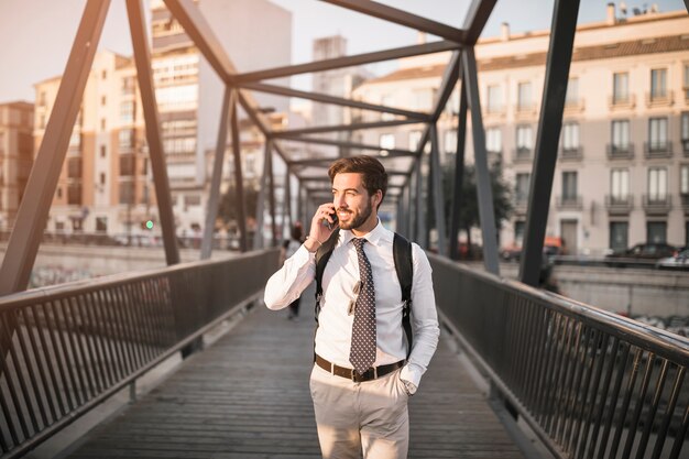 Szczęśliwa młoda męska podróży pozycja na moscie opowiada na telefonie komórkowym