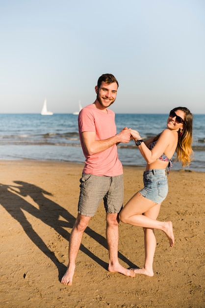 Szczęśliwa młoda para trzymając się za rękę pozowanie na piaszczystej plaży