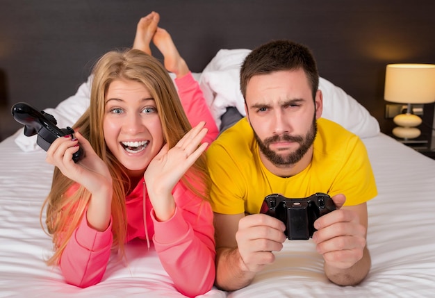 Szczęśliwa młoda para zabawy grając w gry wideo w łóżku.