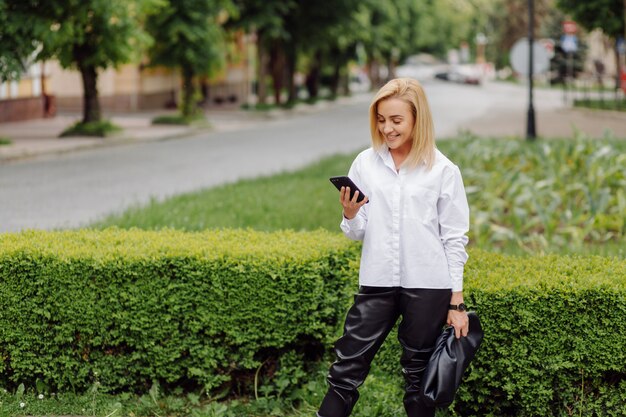 Szczęśliwa młoda piękna kobieta używa jej mądrze telefonu odprowadzenie na miasto ulicie