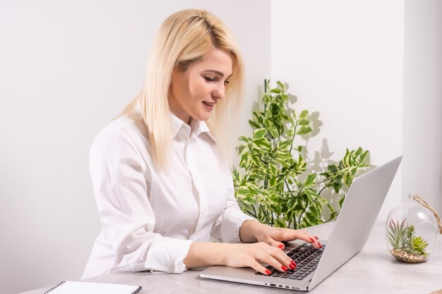 Szczęśliwa młoda piękna kobieta za pomocą laptopa, w pomieszczeniu na tle białej ściany