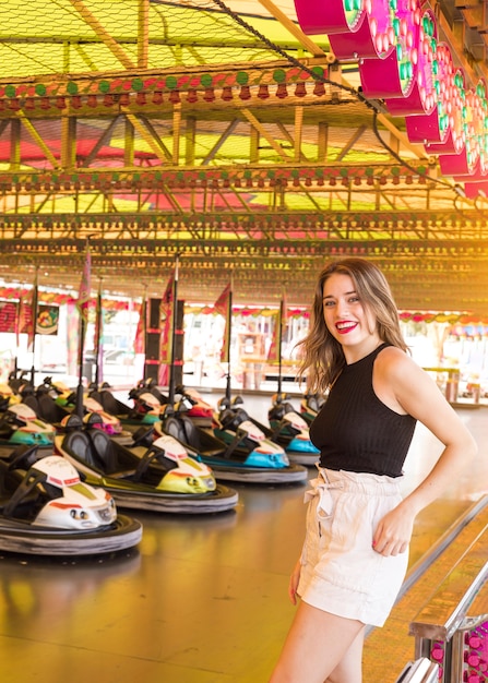 Bezpłatne zdjęcie szczęśliwa młodej kobiety pozycja blisko rekordowej samochodowej przejażdżki przy parkiem rozrywki