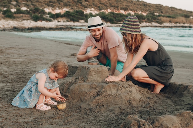 Szczęśliwa modniś rodzina przy plażowym budynku piaska kasztelem