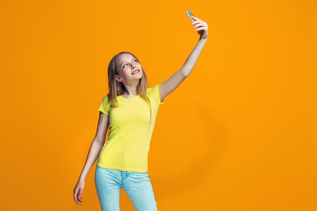 Szczęśliwa nastoletnia dziewczyna stoi i ono uśmiecha się przeciw pomarańcze ścianie