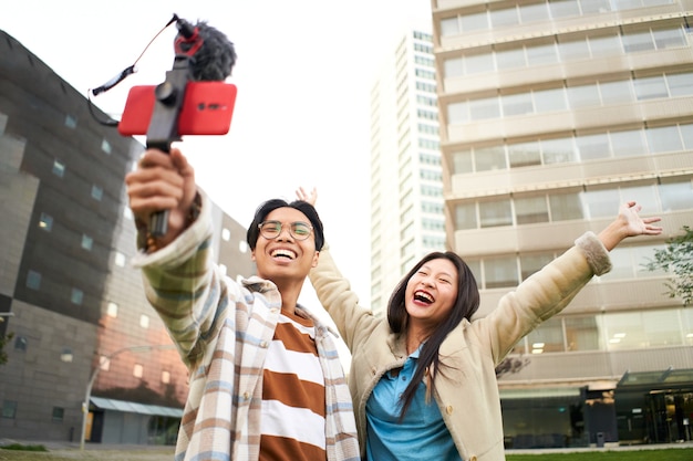 Szczęśliwa para azjatyckich robi sobie selfie w mieście modni młodzi przyjaciele bawią się technologią tr...