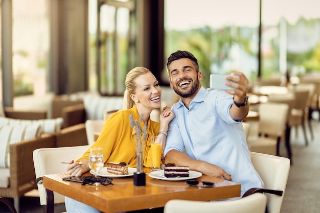 Szczęśliwa para bawi się podczas jedzenia deseru i robienia selfie w kawiarni