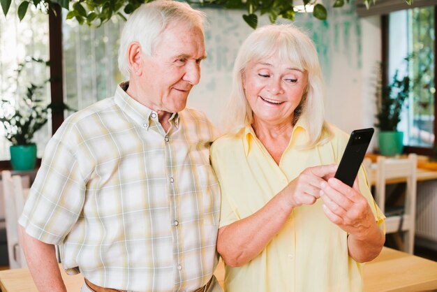 Szczęśliwa para starszy stojący w kawiarni i SMS-y na telefon komórkowy
