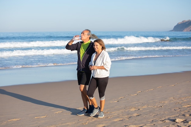 Szczęśliwa para starszych korzystających z aktywnego wypoczynku nad brzegiem morza. Uśmiechnięta kobieta i mężczyzna spacerują razem, oddychając wodą pitną. Szczęśliwe aktywne życie i zdrowie dla osób starszych na emeryturze koncepcja