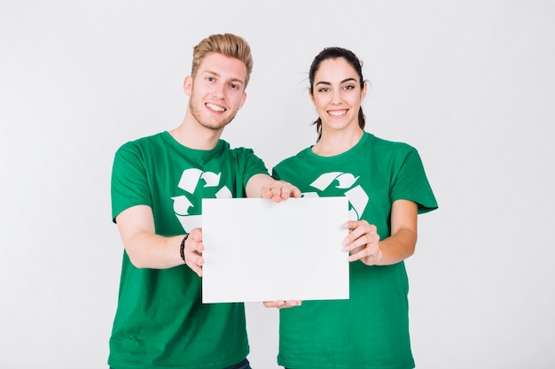 Szczęśliwa para w zielonym koszulki mienia pustym białym plakacie