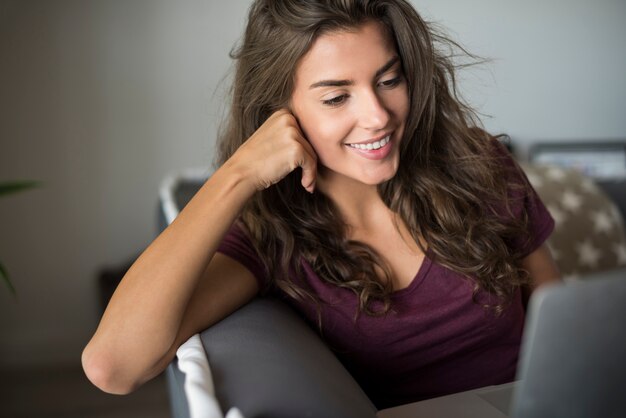 Szczęśliwa piękna młoda kobieta z laptopem w domu