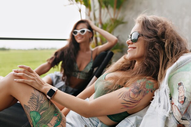 Szczęśliwa piękna stylowa kobieta w dżinsowych szortach siedzi na szezlongu z przyjacielem na letnim tarasie