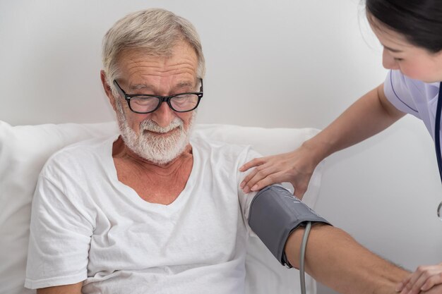 Szczęśliwa pielęgniarka sprawdzająca i mierząca ciśnienie krwi starszego mężczyzny w sypialni w domu opieki
