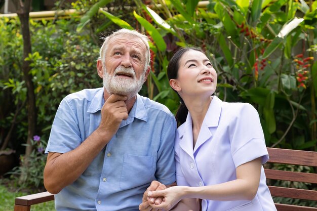 Szczęśliwa pielęgniarka trzyma rękę starszego mężczyzny w ogrodzie w domu opieki, patrząc na niebo