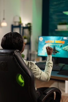 Szczęśliwa podekscytowana kobieta pro gamer siedzi przy biurku w studio gier w domu, grając w gry wideo kosmiczne strzelanki, wygrywając mistrzostwa online. zwycięzca gracza korzystający ze sprzętu komputerowego rgb. cyberprzestrzeń gra