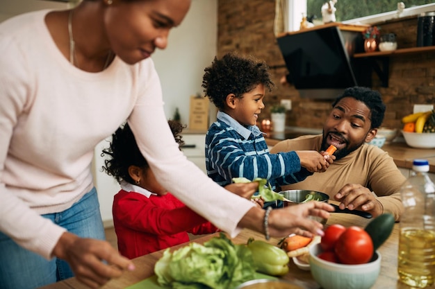 Bezpłatne zdjęcie szczęśliwa rodzina afroamerykanów bawi się podczas przygotowywania zdrowego jedzenia w kuchni